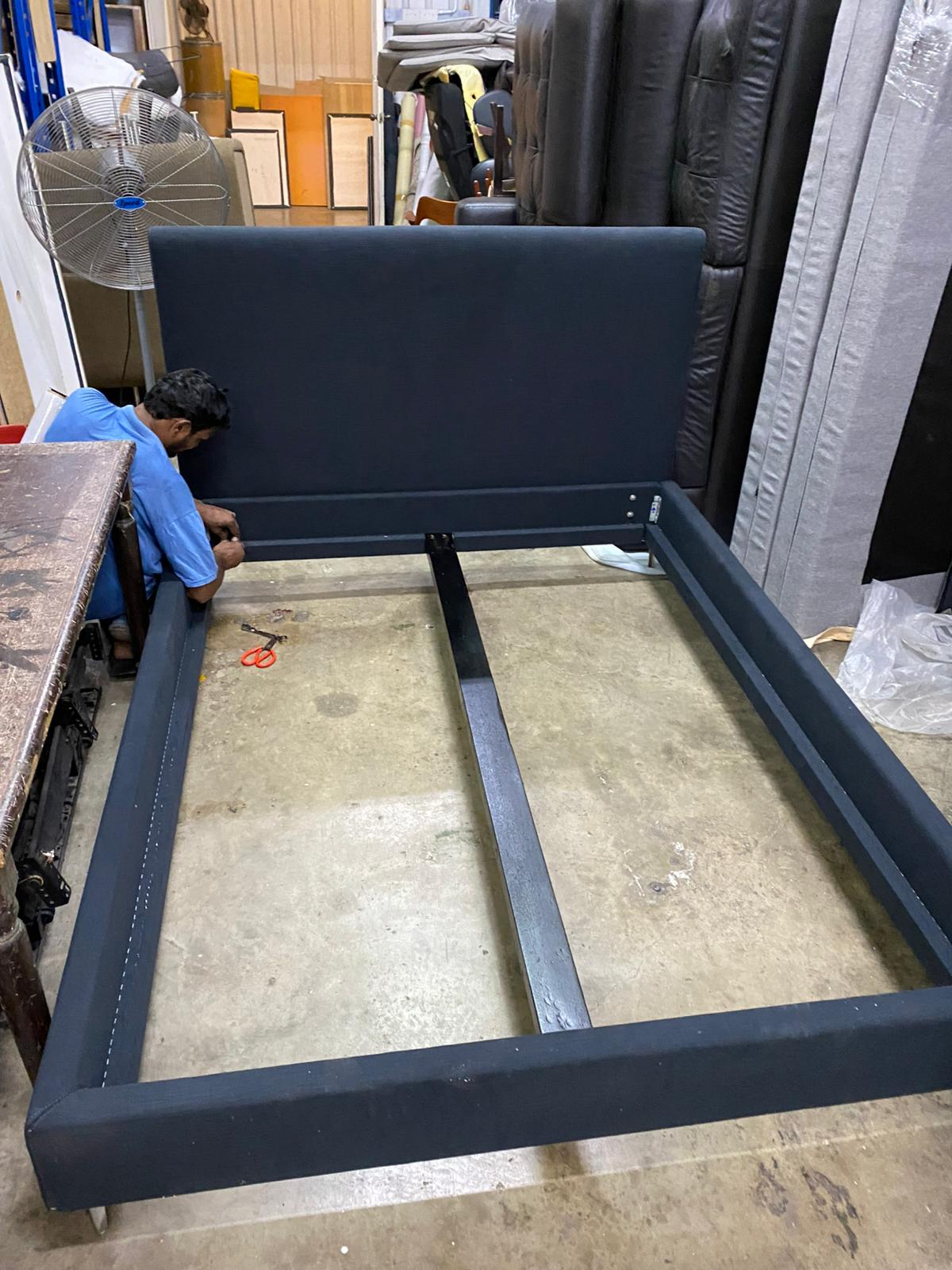Navy fabric upholstered bed frame being assembled by craftsman in workshop